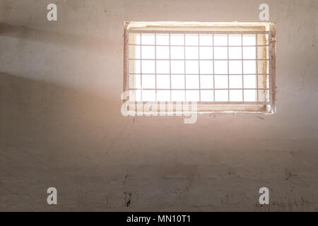 Old white wall with window covered by iron grate. Sun shining  through grill. Mental prison . Enlightment concept. Copyspace Stock Photo