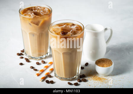 Ice coffee in a tall glass with cream poured over and coffee beans. Cold summer drink on a light blue background Stock Photo