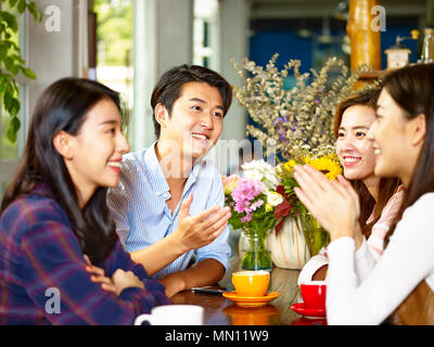 four happy young asian adults men and women chatting talking in coffee shop. Stock Photo