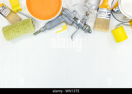 paint brushes, roller, gloves, color samples, paint cans and spray gun on white wooden background. renovation concept. flat view. Stock Photo
