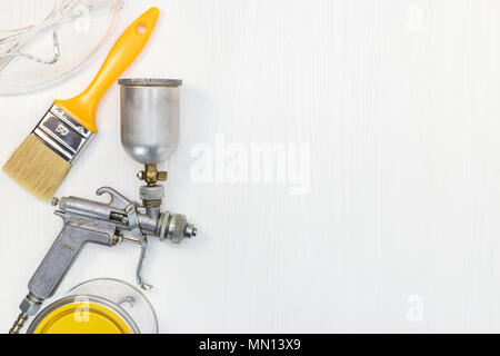 paint can, paintbrush, safety glasses and paint spray gun on white wooden background. top view Stock Photo