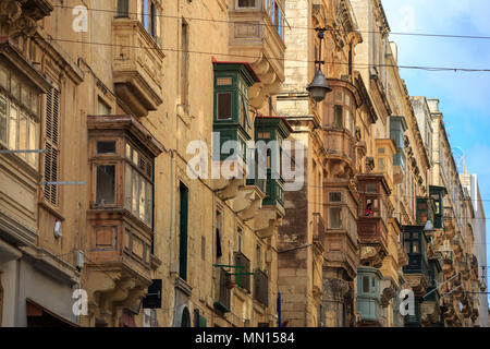 Malta, Valletta, traditional sandstone buildings with colorful wooden windows on covered balconies. Blue sky with clouds background. Close up view. Stock Photo