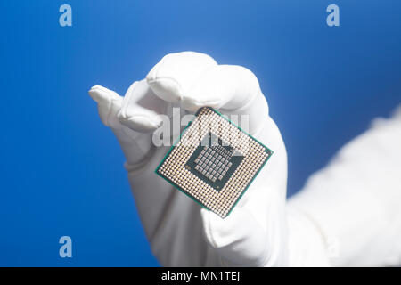 Hand in white glove holding a CPU computer processor microchip on blue background Stock Photo