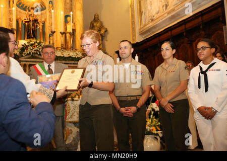 Lieutenant Col. Karin Fitzgerald, the commanding officer for Special Purpose Marine Air-Ground Task Force-Crisis Response-Africa logistics combat element, receives a volunteer appreciation award on the behalf of Marines and Sailors of SPMAGTF-CR-AF LCE from Father Antonio Nicoloso during the Saint Anthony of Padua patron saint festival in Padua, Italy, Aug. 12, 2017. SPMAGTF-CR-AF LCE service members received volunteer appreciation awards during the festival for all the volunteer work they performed throughout the community. SPMAGTF-CR-AF LCE provides logistical support to the entire SPMAGTF-C Stock Photo