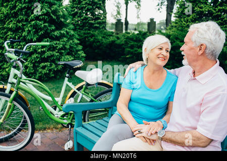 Senior couple relaxing, sitting on park, after riding bicycles. Elderly man and woman are actively resting, retirement Stock Photo