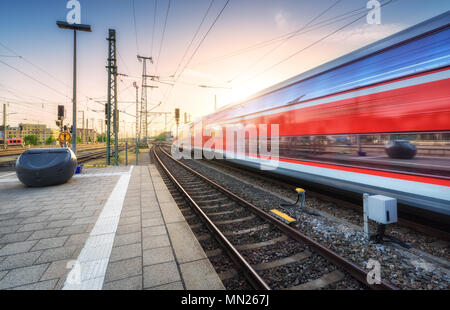 Red high speed train in motion on the railway station at colorful sunset. Germany. Blurred modern intercity train on the railway platform. Passenger t Stock Photo