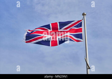 Union Jack flag fluttering in a light breeze on a flagpole against a pale blue sky