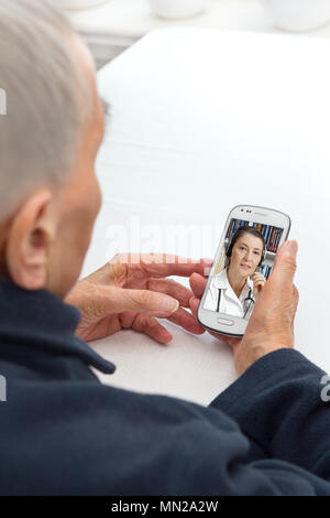 Senior person sitting with her smartphone at a table having a video call with her doctor, modern lifestyle concept Stock Photo