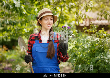 gardener in work clothes holding flower in pot and small spade Stock Photo