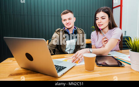 Two colleagues discussing the idea of the project, good-looking boy explaining the main point to lovely brunette, sitting on leather chairs at office desk Stock Photo