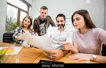 Team of office workers discussing diagrams sitting on working table, indoor shot in modern office Stock Photo
