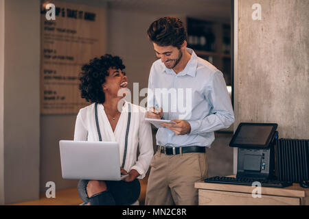 Restaurant owners taking care of finances and payments using laptop and notepad in their restaurant. Man and woman smiling while working at their cafe Stock Photo