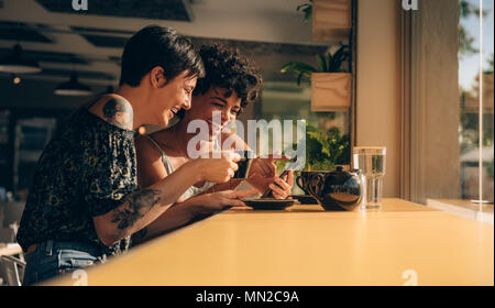Two women using mobile phone and drinking coffee at cafe Females spending their free time at coffee shop. Stock Photo