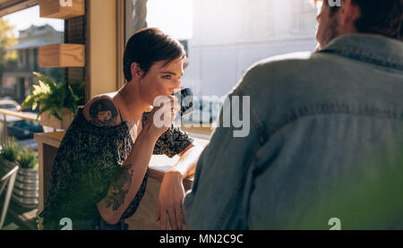 Woman drinking coffee sitting at coffee shop with her male friend. Couple having a cup of coffee at restaurant. Stock Photo