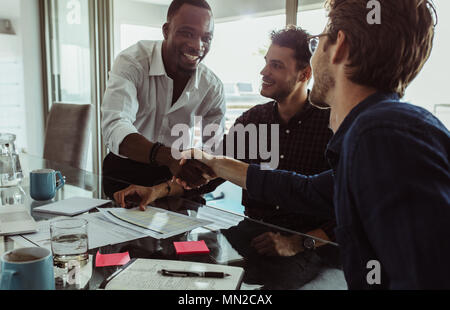 Businessmen discussing work sitting at conference table in office. Men shaking hands and smiling during a business meeting. Stock Photo