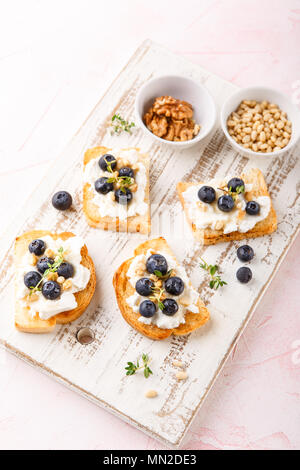 Toast crostini with fresh berries blueberry and honey, Ricotta cheese, thyme and hazelnuts, over white wooden textured board. Top view, copy space. Stock Photo