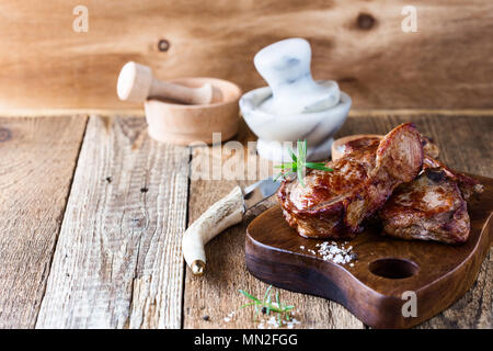 Roasted veal chops with fresh herbs on rustic wooden cutting board, pan seared steak dinner Stock Photo