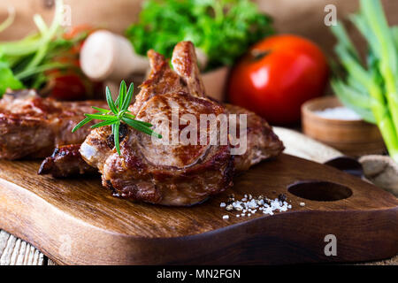 Roasted veal chops with fresh herbs and vegetables on rustic wooden cutting board, pan seared steak dinner Stock Photo