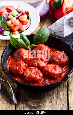 Meatballs in cast iron pan with fresh vegetables and chickpea salad and brown rice on rustic wooden table Stock Photo