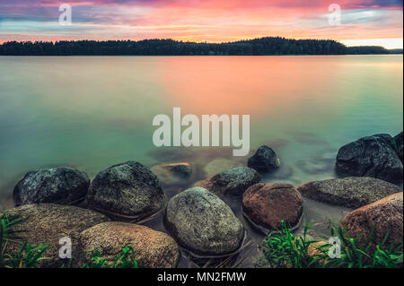 Panoramic view on the lake with dark clouds on the sky and big smooth stones in the front during sunset. Stock Photo