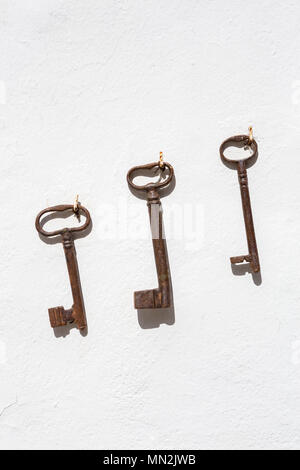 Three old rusty keys hanging in a row on a white wall. Stock Photo