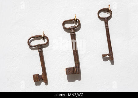Three old rusty keys hanging in a row on a white wall. Stock Photo