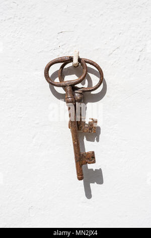 Two old brown rusty keys hanging on a nail against a white wall. Stock Photo