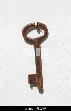An old brown rusty key hanging on a white wall. Stock Photo