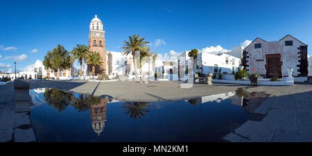 TEGUISE, LANZAROTE, CANARY ISLANDS, SPAIN: A large panorama of the exterior of the church being reflected in a puddle on the square. Stock Photo