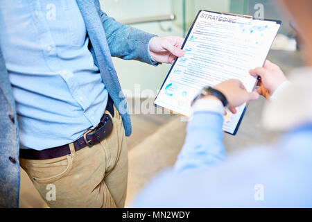 Close up of modern unrecognizable business man holding clipboard with document while discussing strategy with colleague, copy space Stock Photo