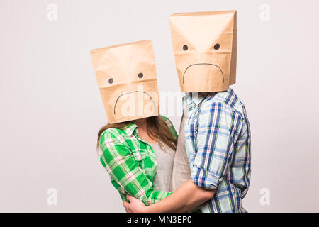 love, family and relationship problems concept - unhappy couple covering their sad faces with paper bag over white background. Stock Photo