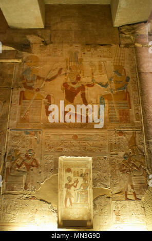 Egypt. Abydos. Temple of Seti I. New Kingdom. 19th Dynasty. Relief with original polychrome, The Second Hypostyle Hall. The Pharaoh Seti I kneeling while he receives emblems from god Amun (wearing two vertical plumes on his head). God Khnum to the left (head of a ram). 1292-1189 BC Stock Photo