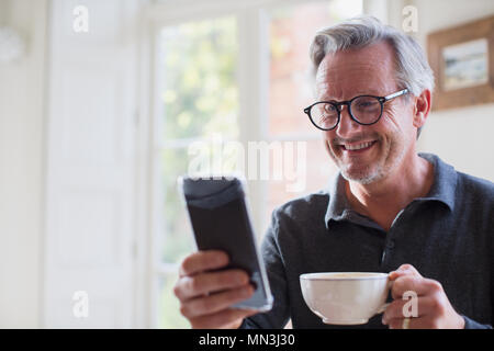 Smiling mature man drinking tea and using smart phone Stock Photo