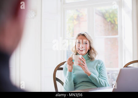 Smiling mature woman drinking tea, talking to man Stock Photo