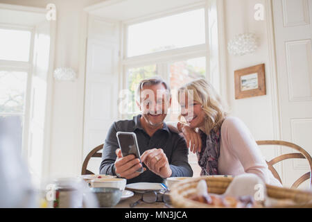 Smiling mature couple using smart phone at dining table Stock Photo