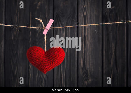 Handmade red heart hanging on rope with clothespin on dark gray wooden background. Happy Valentine's Day celebration. Love message concept Stock Photo