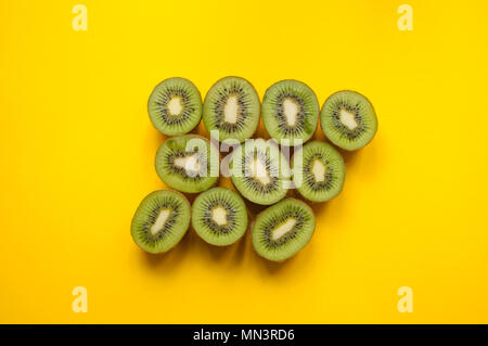 Flat lay of many halves of green kiwi fruit on bright yellow background. Stock Photo