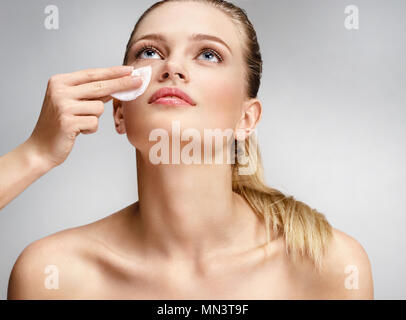 Makeup artist making the face cleaning with a cotton pad. Photo of beautiful woman with natural makeup on grey background. Skin care and beauty concep Stock Photo