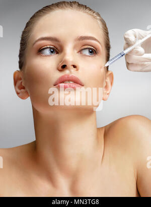 Beautiful woman receiving botox injection in cheek from beautician. Portrait of young woman getting beauty facial injections on grey background. Clean Stock Photo