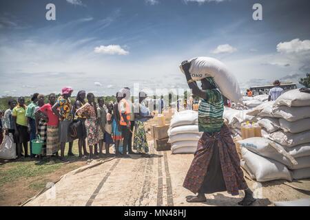May 7, 2018 - Bidi Bidi, Uganda - A female South Sudanese refugees seen carrying a pack of 50 KG of cassava flour on top of the her head while others line up to get their food supplies..The Bidi Bidi refugee settlement in northern Uganda near the South Sudanese border is currently the largest refugee camp in the world, hosting over 250,000 South Sudanese refugees fleeing the conflict. The world food program is providing monthly basic food supply for the refugees in the settlement. (Credit Image: © Geovien So/SOPA Images via ZUMA Wire) Stock Photo