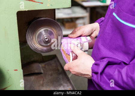 Close-up of a young male worker makes the sole of children's shoes made of genuine leather with a special machine in the sewing workshop Stock Photo
