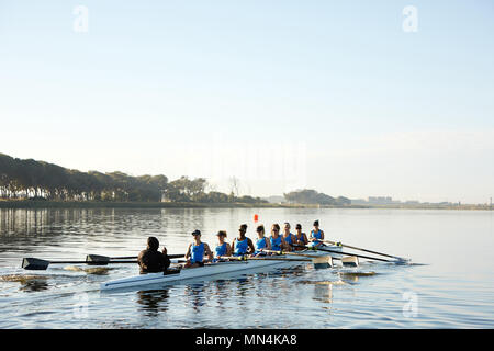 Female rowers rowing scull on lake below blue sky Stock Photo