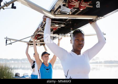 Confident, determined female rowing team lifting scull overhead Stock Photo
