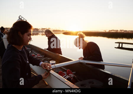 Female rowers preparing scull at sunrise lakeside Stock Photo