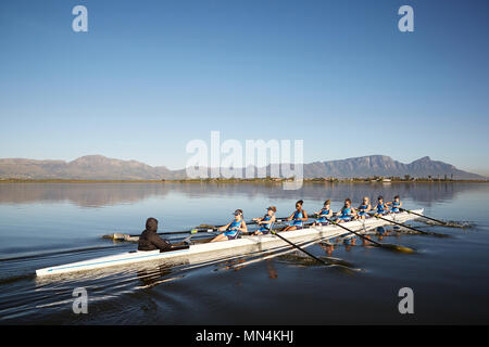 Female rowers rowing scull on sunny lake under blue sky Stock Photo