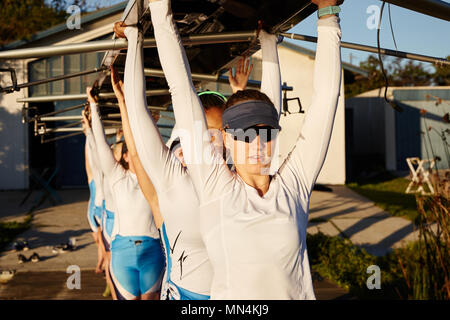 Confident, determined female rowing team lifting scull overhead on sunny dock Stock Photo