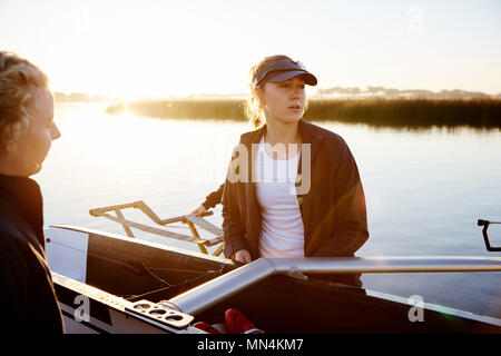 Focused female rower lifting scull at sunrise lakeside Stock Photo