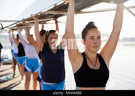 Confident, determined female rowing team lifting scull overhead Stock Photo