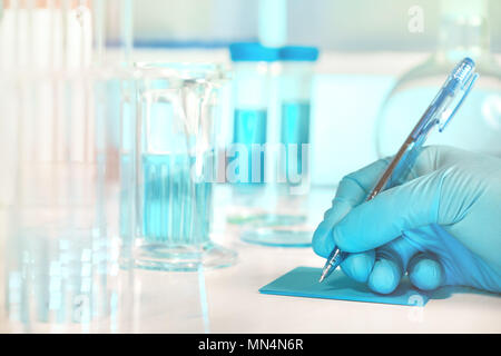 Scientific, medical or education background. Biological or biochemical lab out of focus, closeup on gloved hand writing a note. Focus on the hand. Stock Photo