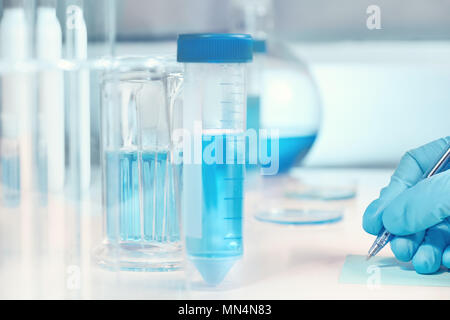Scientific, medical or education background. Biological or biochemical lab out of focus, closeup on gloved hand writing a note. Focus on the hand. Stock Photo